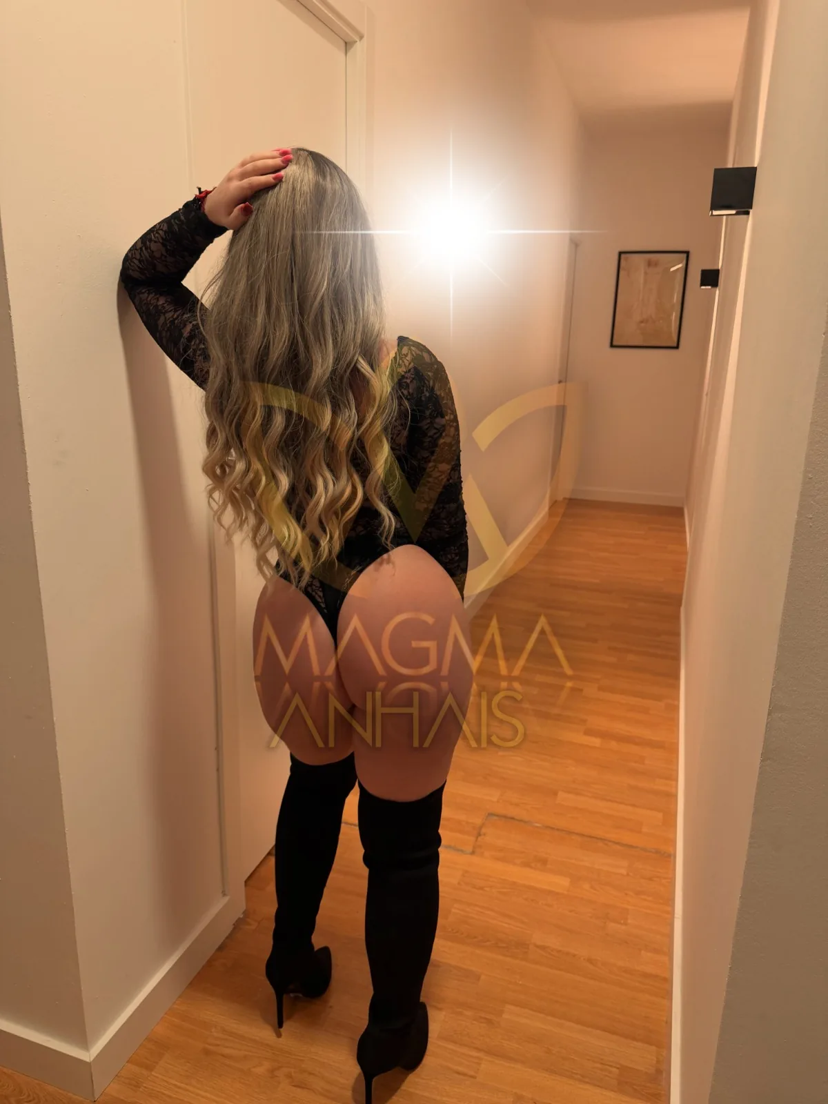 Anhais seen from behind in a white corridor, wearing high boots with one hand on her head.