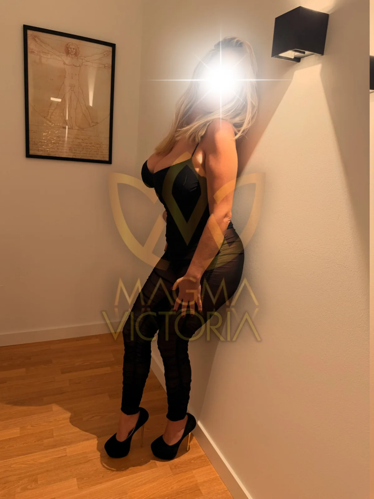 Full-length portrait of Victoria in a black outfit beside a corridor wall.